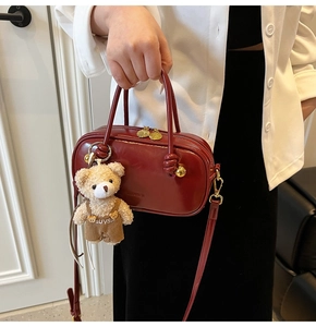 Detail of burgundy Boston bag featuring knotted handle and a cute teddy bear charm