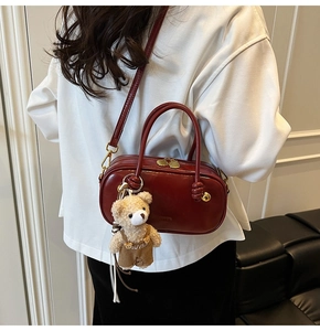 Detail of burgundy Boston bag with golden zipper charm and brown teddy bear pendant