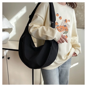 Close-up of a black minimalist crescent bag with a wide strap on a model shoulder