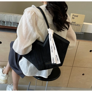 Detail showing black corduroy tote bag with fashion tag and decorative logo ribbon