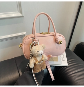 Pink leather Boston bag featuring a brand logo, cross-body strap, and bear doll charm