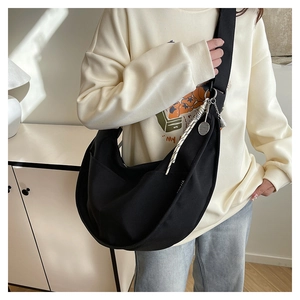 Detail of black canvas crescent bag featuring wide strap, outer pocket and woven tassel