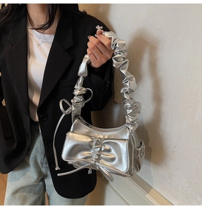 Dettaglio della borsa metallizzata argento con fiocco pieghettato e manico arricciato