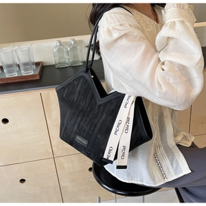 Detail of black velvet tote bag featuring V-cut top edge and white lettered strap