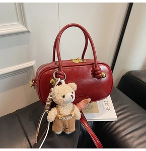 Close-up of deep red leather Boston bag with gold hardware and a cute plush bear charm