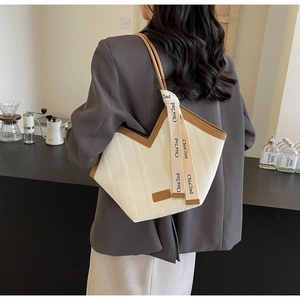 Detail of a large contrast tote bag with branded ribbon strap worn by a model