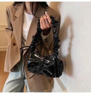 Dettaglio borsa in pelle verniciata nera lucida con manico a pieghe e decorazione a fiocco