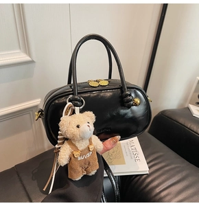 Detail of black glossy leather Boston bag with gold zipper and plush bear charm