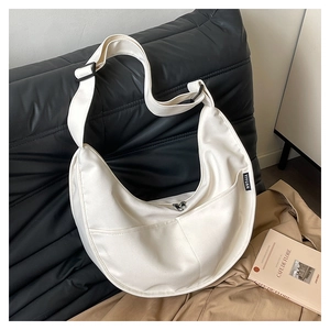 Detail of a beige canvas half-moon hobo bag featuring a front pocket and woven brand label
