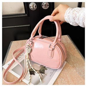 Pink leather bowling bag with heart charm and woven tassel detail being held by hand