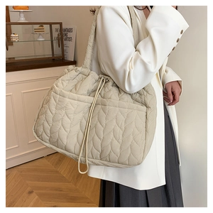 Detailed shot of cream quilted tote bag with drawstring and leaf pattern on a model
