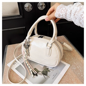 Close-up of cream glossy bowling bag featuring woven charm and metal key pendant details
