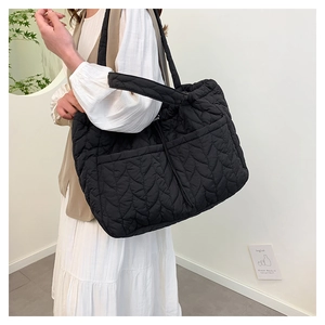Close-up of black quilted tote bag with wavy stitching and front functional pocket