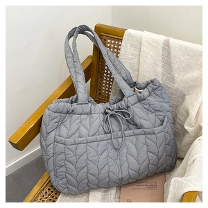 Detail of grey quilted tote bag with drawstring closure on a wooden chair