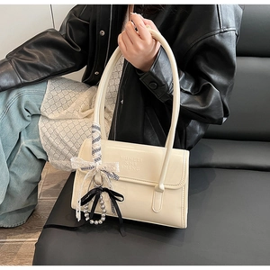 Détail du sac sous le bras crème avec lettres embossées et breloque noeud en perles