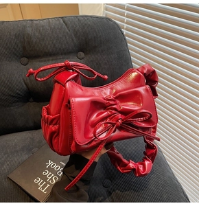 Dettaglio borsa in pelle verniciata rossa con fiocco e manico increspato su velluto