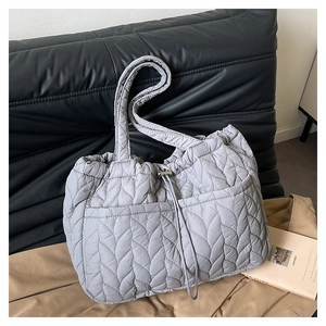 Detail of grey leaf-quilted shoulder bag with drawstring closure on textured background