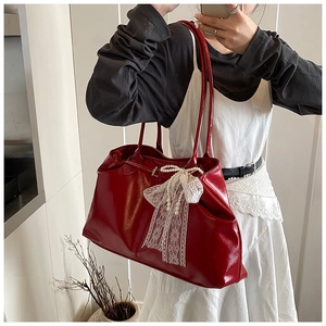 Detail of red tote bag featuring large white lace bow and elegant pearl tassel accents