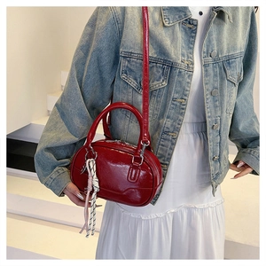 Close-up of glossy burgundy patent leather bowling bag with braided charm detail