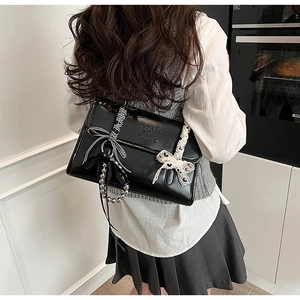 Détail du sac bandoulière en cuir noir avec nœud en dentelle et perles en métal