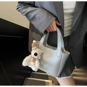 Detail of silver lychee texture leather bucket bag featuring a cute teddy bear charm