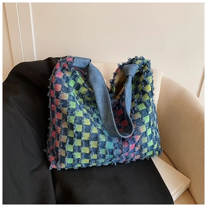 Detail of multi-color plaid tweed tote bag with fringe edges and blue denim shoulder strap