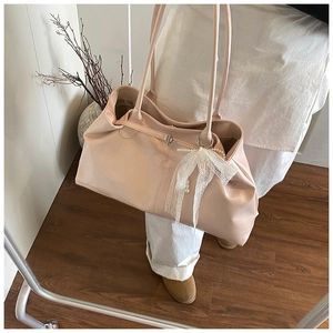 Detail of a large beige tote bag featuring a decorative lace bow and pearl pendant charm