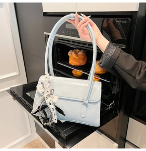 Détail d'un sac à main en cuir verni bleu clair avec ruban à nœud et breloque en perle