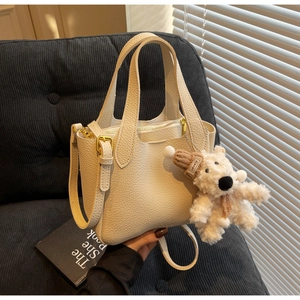 Close-up of beige lychee texture leather bucket bag with a cute white plush bear pendant