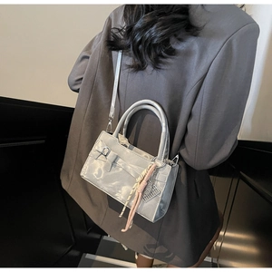 Dettaglio di borsa grigia in pelle verniciata con fiocco e ciondolo su blazer grigio