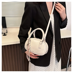 Detail view of cream mini bowling bag with woven charm and adjustable shoulder strap