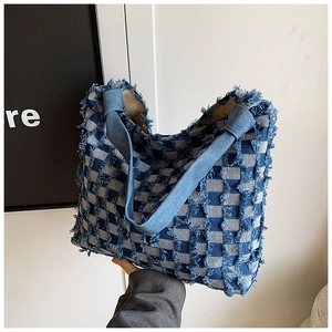 Detail of blue and white checkered denim tote bag featuring frayed tassel texture
