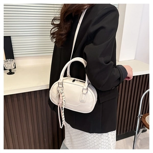 Detail of off-white PU leather bowling bag showing side texture and woven rope charm