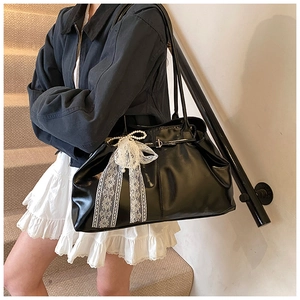 Close-up of black glossy tote bag featuring delicate white lace bow and pearl charms