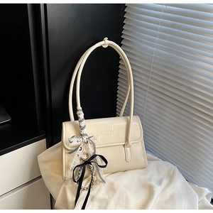 Détail d'un sac sous le bras en cuir blanc crème avec un nœud à carreaux et perles en métal