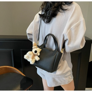 Detail of black lychee grain leather bucket bag with a cute plush dog pendant