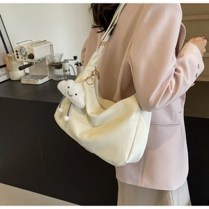 Detail view of a cream crescent hobo bag with a plush cloud charm on a wide shoulder strap
