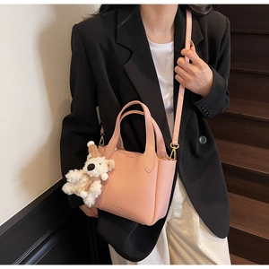 Pink lychee texture bucket bag with plush bear charm shown on a wooden staircase