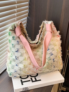 Colorful plaid woven tote bag with fringe details and a pink strap on a stylish display