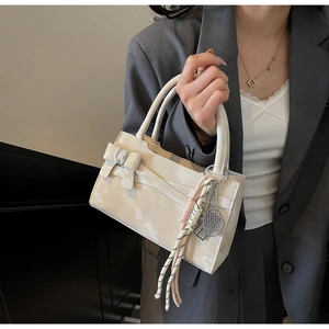 Dettaglio della borsa bianco crema con fiocco e ciondolo a racchetta indossata con blazer