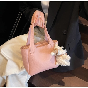 Detail of pink lychee leather bucket bag with a cute plush dog charm on a wooden stair