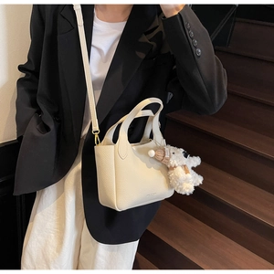 Close-up of cream white lychee texture bucket bag with a cute plush puppy pendant