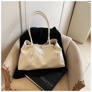 Detail of a creamy white tote bag featuring lace bow and pearl pendant on a matte leather surface