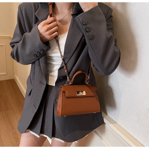 Detailed close-up of brown litchi grain leather bag with golden twist lock and chain strap