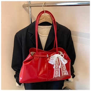 Detail of red patent leather tote bag featuring a white lace bow with pearl accent