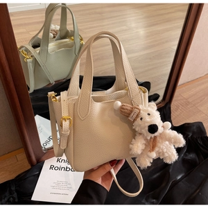 Detail of lychee pattern leather bucket bag with gold hardware and plush bear charm
