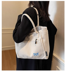 Detail view of a cream canvas tote bag with TCT lettering shown on model shoulder