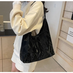 Macro shot of large black hobo tote bag featuring wrinkled glossy leather and minimalist design
