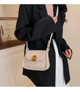 Close-up of minimalist cream saddle bag with vintage bronze U-shaped buckle and strap