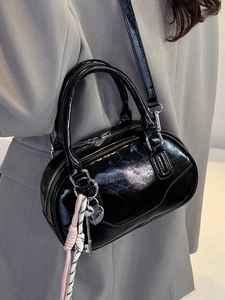 Chic black glossy bowling bag with heart charm and crossbody strap worn by model